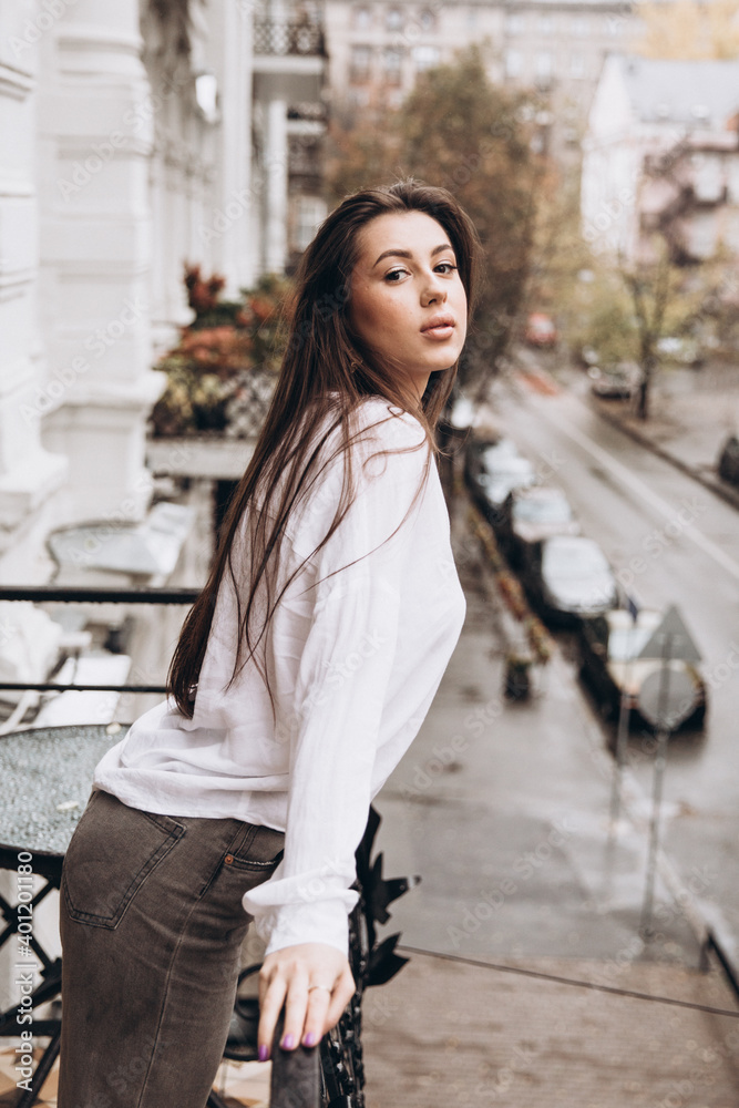 Fototapeta premium Photoshoot of a beautiful girl in a white shirt on the balcony