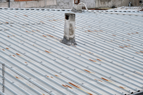 Roof of house made of metal panels. Corrosion exists on roof and old style chimney stack during overcast weather.