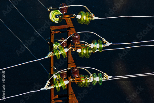 Glass electric insulators mounted on wires of old rusty powertower view from above