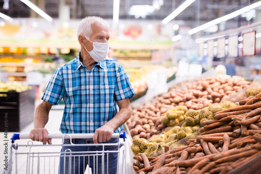 mature caucasian man in mask with covid protection choosing potatoes in vegetable section of supermarke