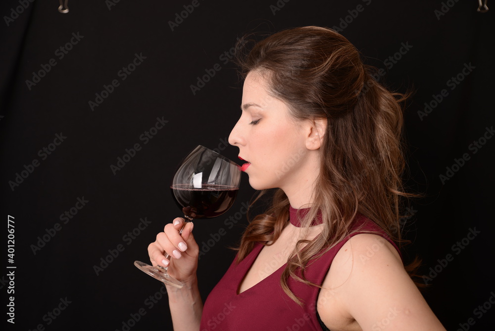 girl with red lips in a Marsala dress holding a glass of red wine in her hands on a black background girl with red lips in a Marsala dress holding a glass of red wine in her hands on a black background