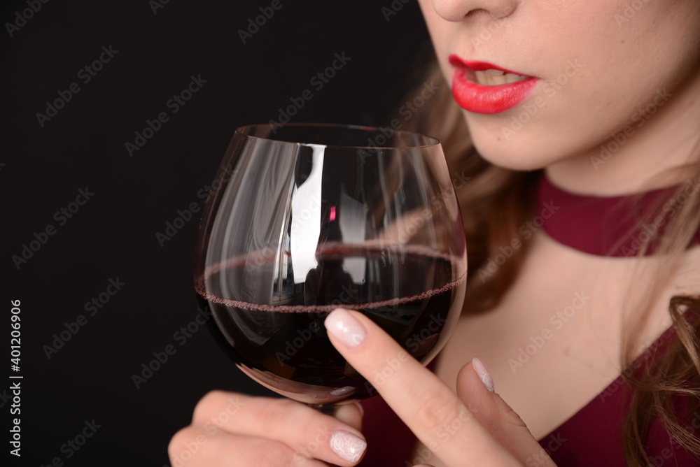 girl with red lips in a Marsala dress holding a glass of red wine in her hands on a black background girl with red lips in a Marsala dress holding a glass of red wine in her hands on a black background