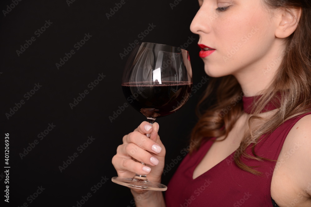 girl with red lips in a Marsala dress holding a glass of red wine in her hands on a black background girl with red lips in a Marsala dress holding a glass of red wine in her hands on a black background