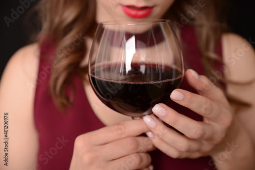 girl with red lips in a Marsala dress holding a glass of red wine in her hands on a black background