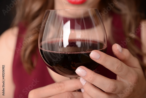 girl with red lips in a Marsala dress holding a glass of red wine in her hands on a black background