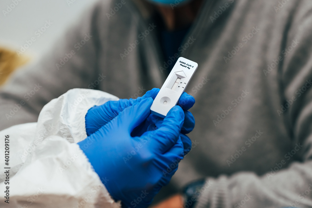 Close up of doctor hands with protective gloves and PPE suit, showing a test device to senior patient. Review of a Rapid Antigen Test for SARS Covid-19. Close up of doctor hands with protective gloves and PPE suit, showing a test device to senior patient. Review of a Rapid Antigen Test for SARS Covid-19.