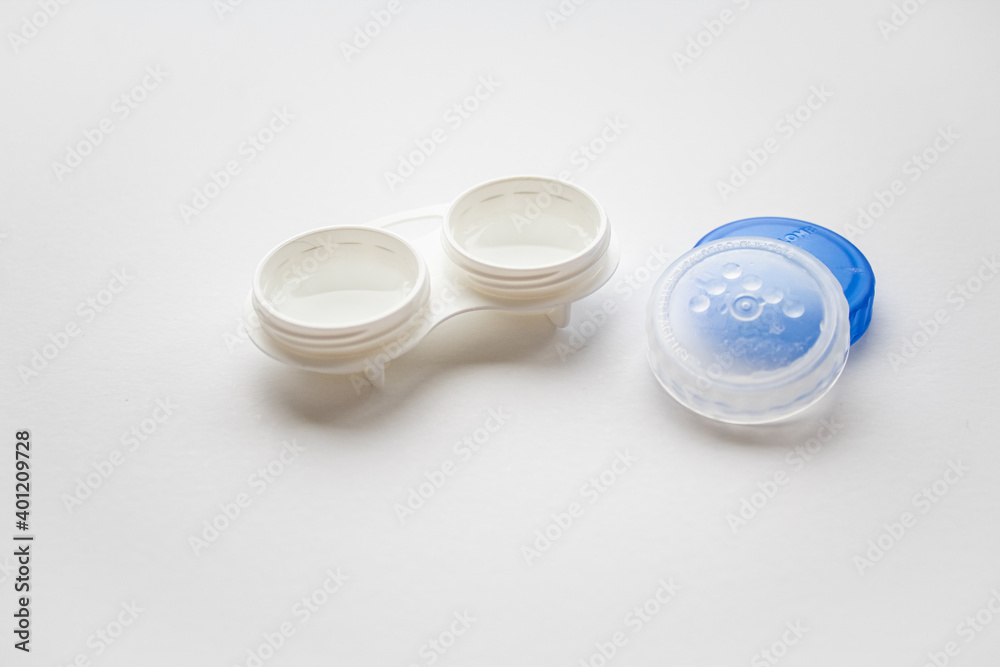 An open white container for lenses next to lie the lids 