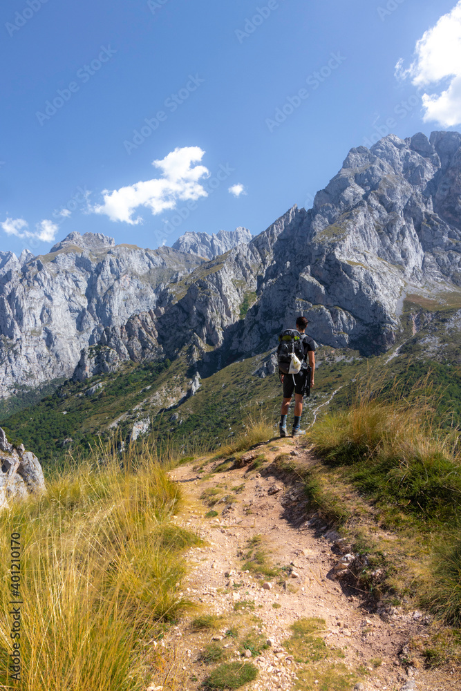 Hombre joven senderista contemplando las vistas de las montañas en el parque nacional de los picos de europa dirigiendose a collado jermososo.