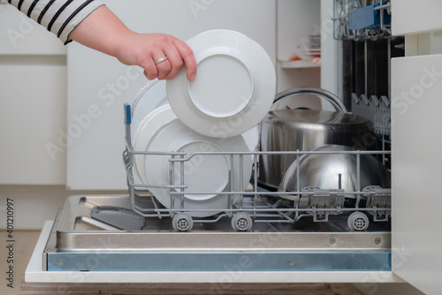 Close up of hand unloading dish washer in the kitchen. Person taking of appliances of full shelf of dishwasher.