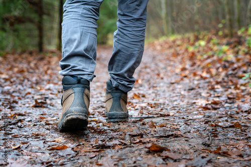 Close up of hiker walking down the wet forest path. Person with dirty hiking shoes on the footpath outdoors. © CrispyMedia