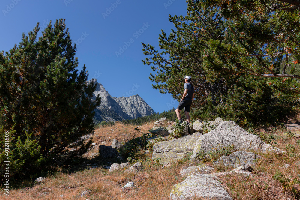 Hombre joven caucásico senderista encima de una roca contemlando las vistas de los picos al fondo en el parque nacional de Aiguestortes camino al Refugio Josep Maria Blanc