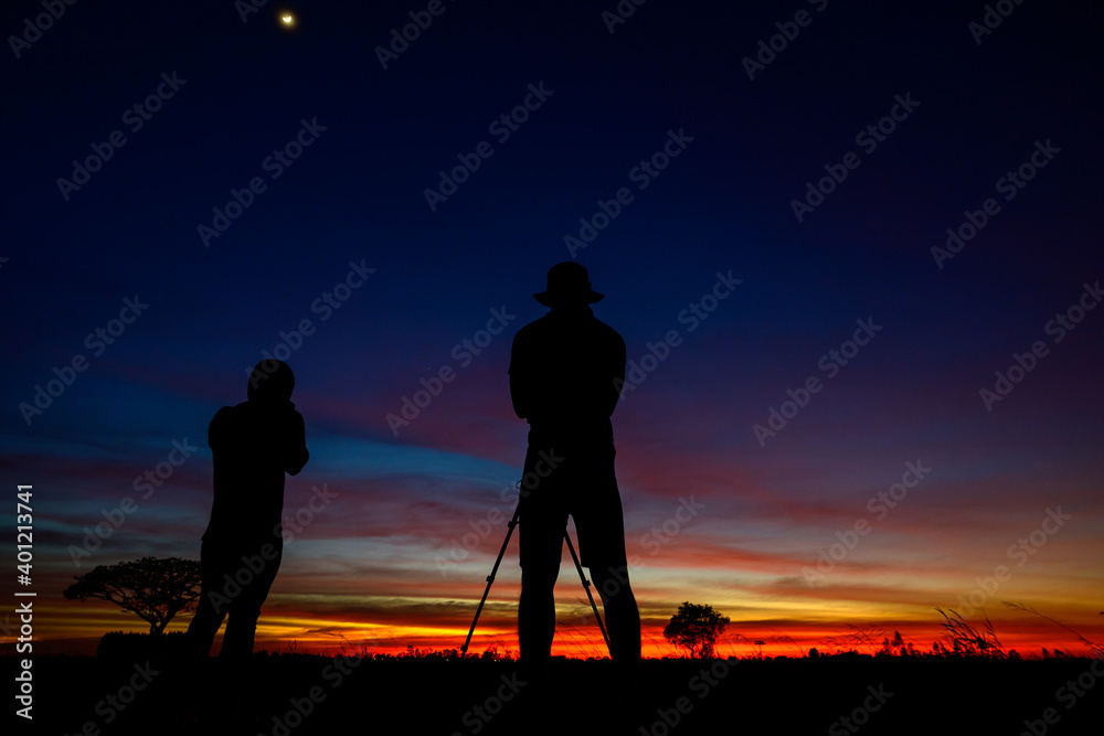 Fototapeta premium Silhouette of couple photographer standing on open field at sunset background.