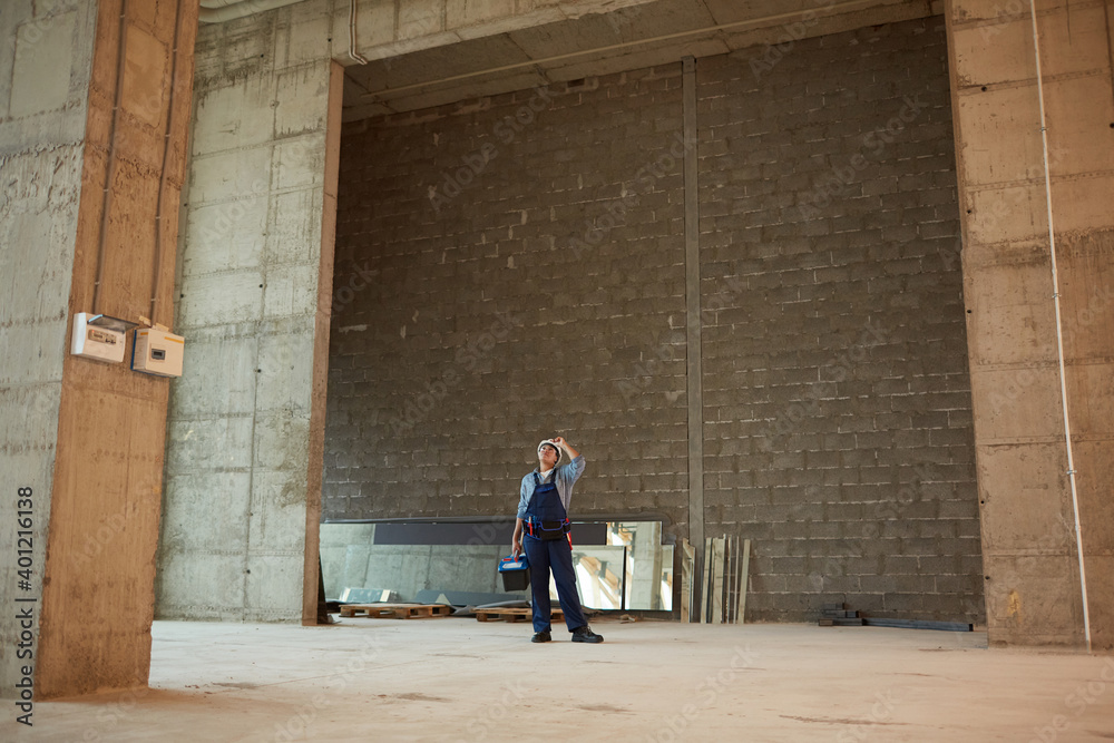 Fototapeta premium Wide angle view of female construction worker wearing hardhat while standing in big concrete archway, copy space