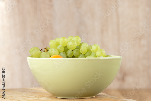 A bunch of green grapes in a deep bowl stands on a wooden table