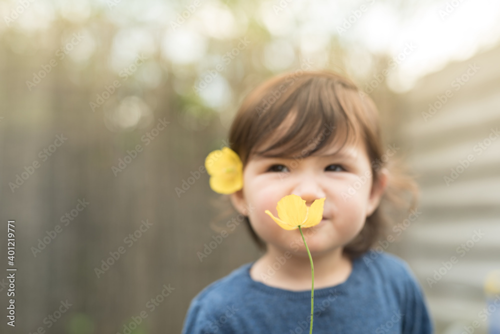 A toddler with a yellow flower on her hair holds another yellow flower in front of her face and smiles as she smells it in the garden of a house in Edinburgh, Scotland, United Kingdom A toddler with a yellow flower on her hair holds another yellow flower in front of her face and smiles as she smells it in the garden of a house in Edinburgh, Scotland, United Kingdom