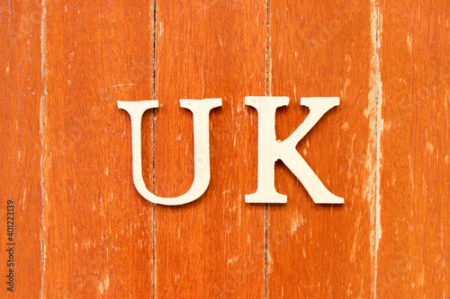 Alphabet letter in word UK (abbreviation of united kingdom) on old red color wood plate background