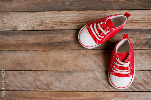 Cute red baby girl sneakers on brown wooden background with copy space