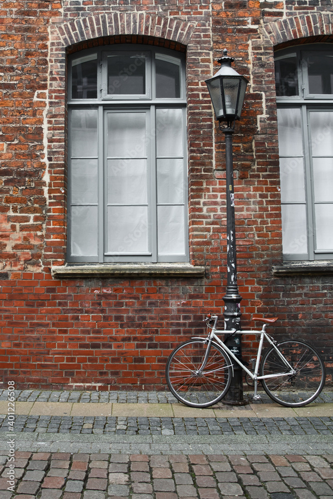 White bicycle tied to a streetlamp in front of a brick wall