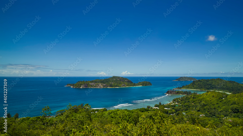 Panoramic view of the densely overgrown green Seychelles washed by turquoise water, the horizon is buried in the sea.
