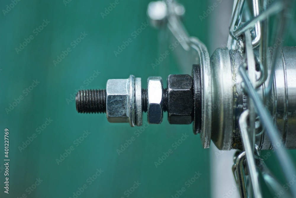 fragment of a bicycle made of black iron sprocket on a wheel with a bolt and gray nuts on a green background fragment of a bicycle made of black iron sprocket on a wheel with a bolt and gray nuts on a green background