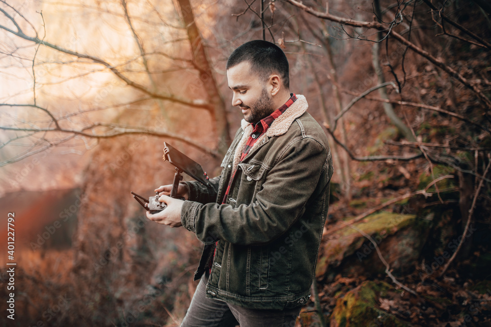 Young smiling drone operator piloting a Drone In A Mountain Over A Lake Autmn Scenery. Young smiling drone operator piloting a Drone In A Mountain Over A Lake Autmn Scenery.