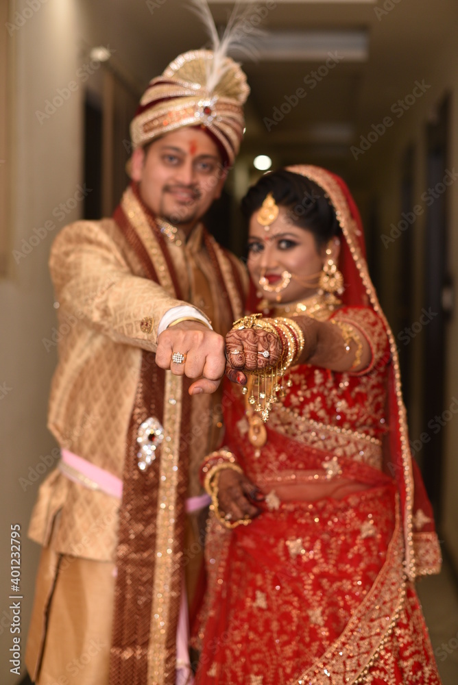 Young Indian Bride groom posing for photograph and flaunting their wedding ring. The couple is wearing traditional indian wedding dress which is designer red lehenga for bride and sherwani for groom.