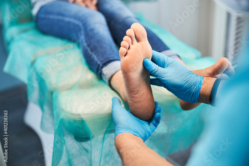 Unrecognized chiropodist on blue gloves examining toes and feet of female patient in medical center photo