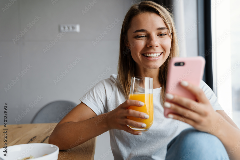 Beautiful happy girl using mobile phone while drinking juice