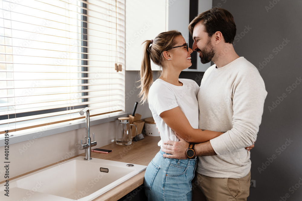 Beautiful happy caucasian couple laughing and hugging at home kitchen Beautiful happy caucasian couple laughing and hugging at home kitchen