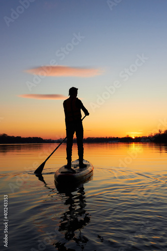 Foto Rear view on silhouette of stand up paddle boarder paddling at sunset on river a