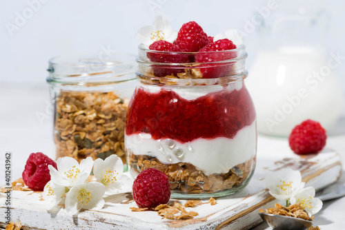 sweet desserts with granola, and raspberries puree in jar on white wooden board, closeup