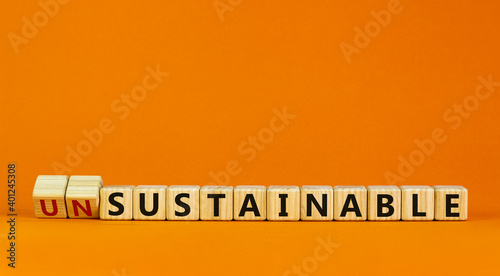 Sustainable or unsustainable symbol. Turned a cube and changed word 'unsustainable' to 'sustainable' on wooden cubes. Beautiful orange background, copy space. Business and sustainable concept. photo
