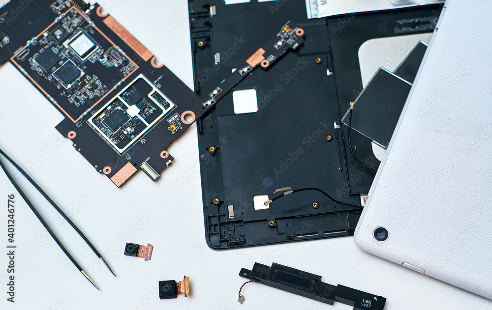 Disassembled PC tablet on the desktop on a white background. A pair of tweezers. PC tablet web cameras.