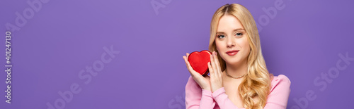 blonde young woman holding red heart shaped box isolated on purple, banner. © LIGHTFIELD STUDIOS