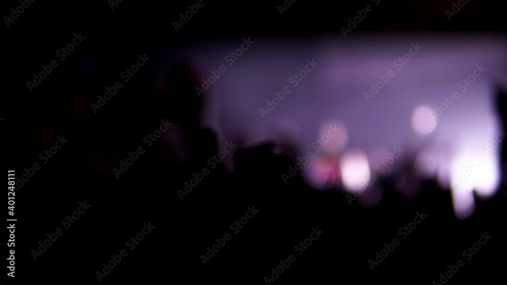 Blur footage of music festival at night club in slow motion. Defocused video of dancing and jumping people with hands up at a concert illuminated by flashing lights. Close-up of fans at a performance.