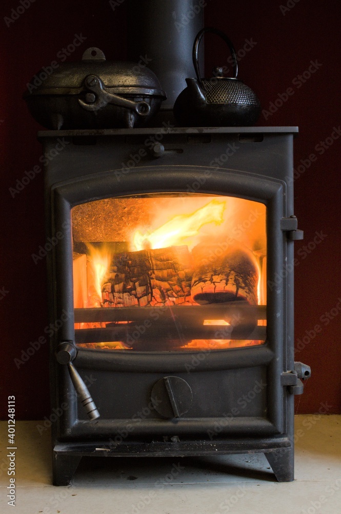 Close up of a log burner glowing with a kettle and potato baker on the top Close up of a log burner glowing with a kettle and potato baker on the top