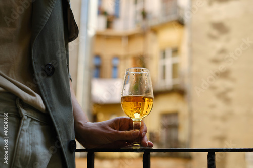 Beautiful girl with a wine glass on the balcony. Drinks white wine and enjoy the moment. A celebration holiday alone. Relaxed lifestyle. Happy woman rest after work. Beautiful European courtyard