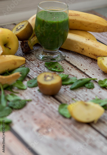  A glass of kiwi, spinach and apple smoothie. Health drink. Apples, flax seeds, spinach, kiwi, bananas lie nearby.