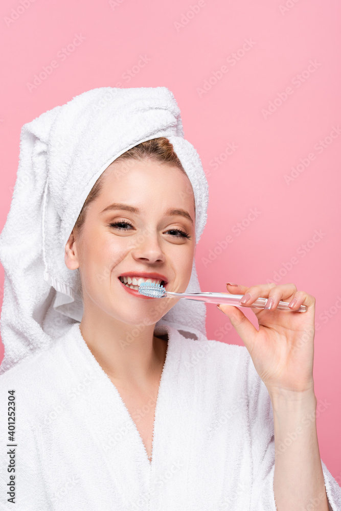 smiling young woman in bathrobe with towel on head brushing teeth isolated on pink. smiling young woman in bathrobe with towel on head brushing teeth isolated on pink.
