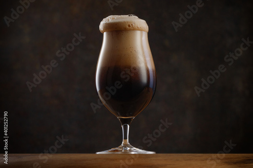 Glass of Dark beer with overflowing foam head.