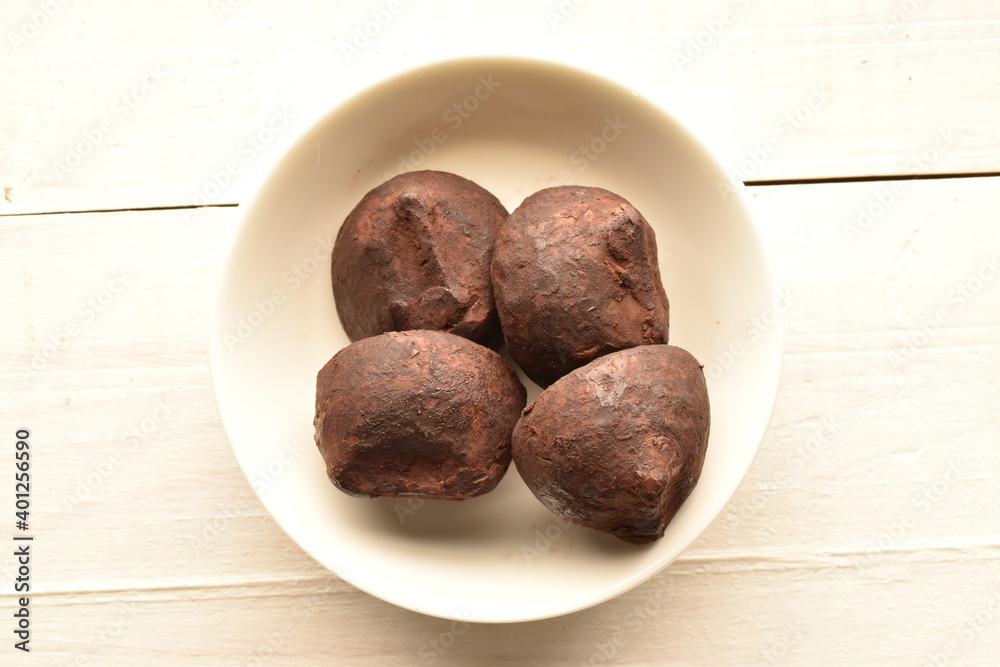 Several delicious chocolate truffles on a white ceramic dish, close-up, on a white wooden table. Several delicious chocolate truffles on a white ceramic dish, close-up, on a white wooden table.