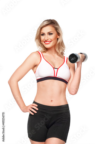 Portrait of a fit, young white female athlete with curly long blond hair posing by herself holding a dumbbell in a studio with white background wearing black shorts & sports bra.