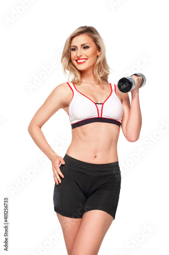 Portrait of a fit, young, laughing white female athlete with curly long blond hair posing by herself holding a dumbbell in a studio with white background wearing black shorts & sports bra.