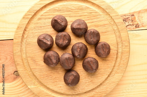 Several delicious chocolate truffles on a round wooden tray, close-up, on a wooden table.