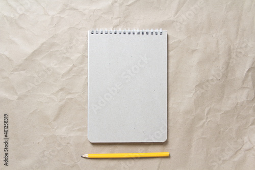  Gray notepad with white coiled spring and pencil on a background of beige crumpled craft paper