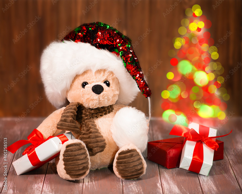 Teddy bear in santa hat with gifts and christmas tree.