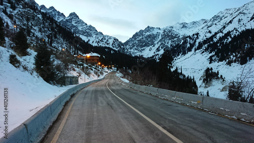 The building of the snowy mountains and forests. Dawn. Lanterns are lit, the road goes into the gorge. The high peaks are completely covered with snow. Almaty, Shymbulak ski resort, Kazakhstan.