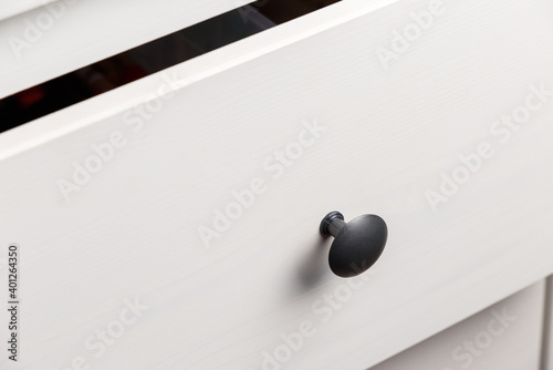 Black handle on white wooden chest of drawers. Minimalism. Minimal concept. Close-up. The texture of natural wood