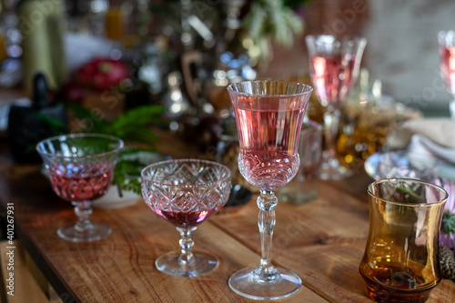 a variety of crystal glasses with rose wine, plates, candlesticks and other vintage staff in a mess on a wooden table