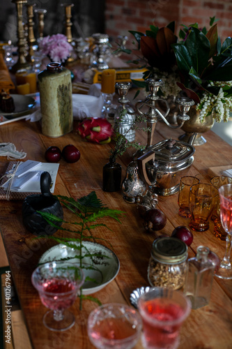 a variety of crystal glasses with rose wine, plates, candlesticks and other vintage staff in a mess on a wooden table © Dana Keli